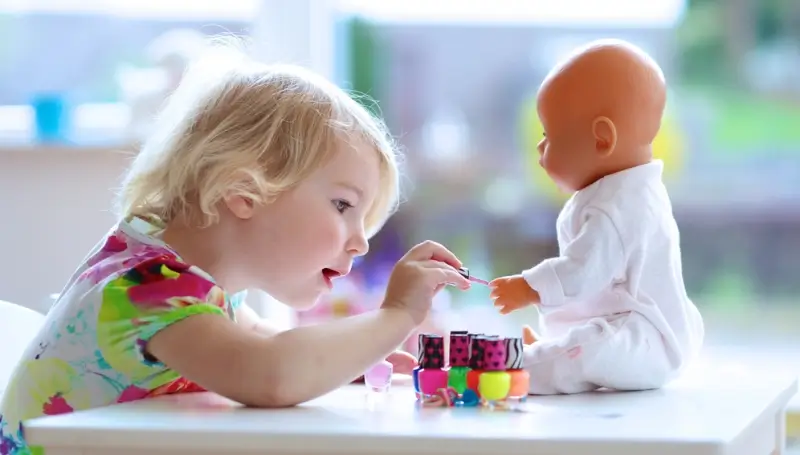 Little girl painting her doll’s nails during imaginative doll play