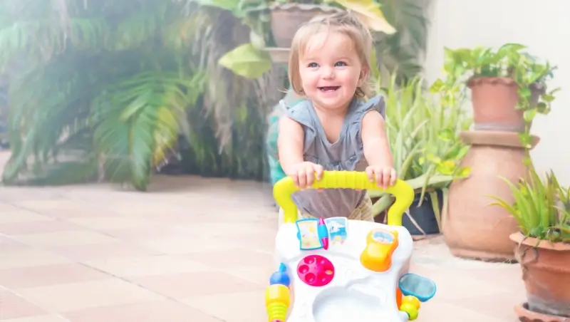 Young girl using a push toy as an alternative to a baby walker while learning to walk